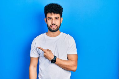 Sakallı, beyaz tişörtlü genç bir Arap adam endişeli, endişeli ve şaşırmış bir ifade takınıyor. 