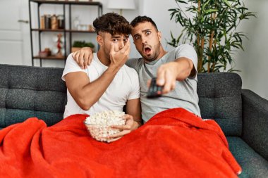 Evdeki kanepede oturup film izleyen iki İspanyol erkek.