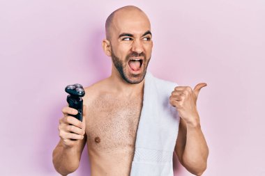 Genç kel adam elinde elektrikli jiletle baş parmağını kaldırmış ağzı açık gülümsüyor. 