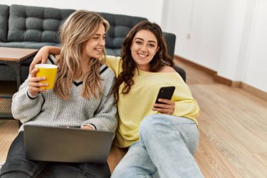 Laptop ve akıllı telefon kullanan genç bir çift evde kahve içiyor..