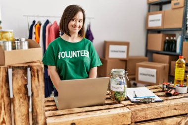 Down sendromlu esmer kadın bağış standında dizüstü bilgisayar kullanıyor.