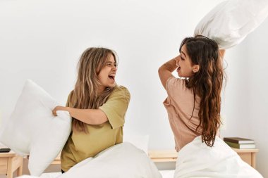 Mutlu gülümseyen genç çift evdeki yatakta yastıklarla kavga ediyor..