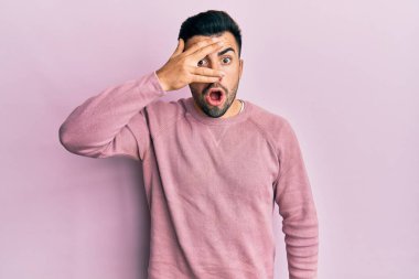 Gündelik kıyafetler giyen genç İspanyol adam şok içinde yüzünü ve gözlerini eliyle kapatıyor, parmaklarından korkuyla bakıyor. 