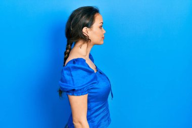 Latin kökenli genç bir kız günlük giysiler giyiyor. Yan tarafa bakıyor, rahat poz veriyor, kendine güvenen bir gülümsemeyle doğal bir yüz ifadesi sergiliyor.. 