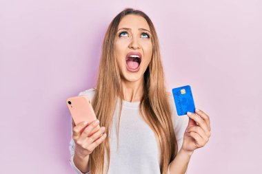Akıllı telefon ve kredi kartı tutan genç sarışın kız kızgın ve kızgın çığlık atıyor sinirli ve öfkeli, öfkeyle bağırıyor.. 
