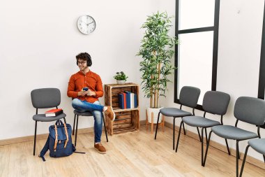 Genç İspanyol adam, bekleme odasında müzik dinlerken kendinden emin bir şekilde gülümsüyor.