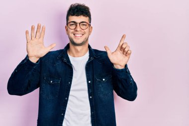 Gündelik kıyafetler giyen ve gözlük takan genç İspanyol adam yedi numaralı parmaklarını gösterip işaret ederken kendine güvenen ve mutlu bir şekilde gülümsüyor.. 