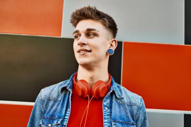 Duvara yaslanmış gülümseyen beyaz bir genç.