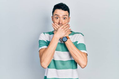 Gündelik kıyafetler giyen genç İspanyol adam yanlışlıkla elleri ile ağzını kapatırken şok oldu. gizli kavram. 