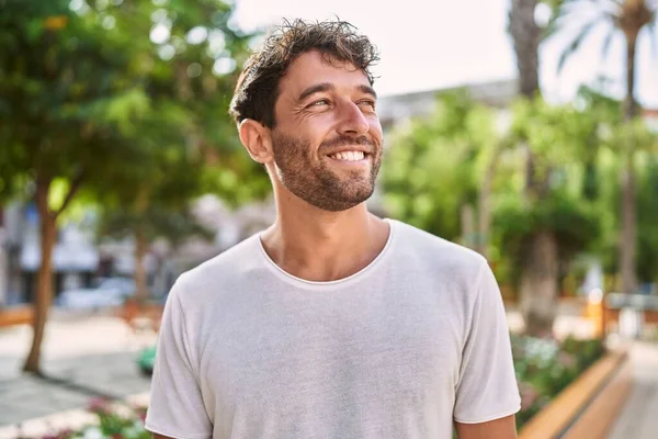 Genç İspanyol adam parkta yürürken kendinden emin gülümsüyor.