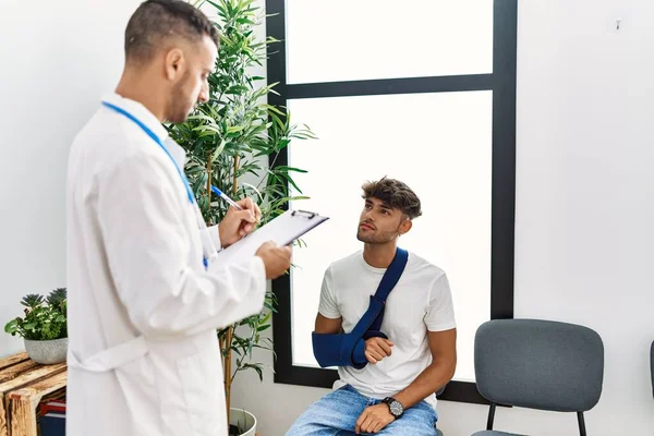 Zwei Hispanische Männer Arzt Und Patient Schreiben Auf Klemmbrett Sitzt — Stockfoto