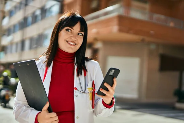 城市里穿着医生制服的年轻黑发女人用智能手机 — 图库照片