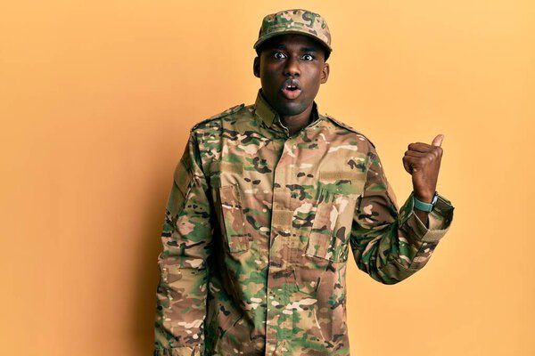 Young african american man wearing army uniform surprised pointing with hand finger to the side, open mouth amazed expression. 