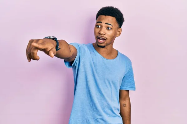 若いアフリカ系アメリカ人の男を着てカジュアルブルーTシャツを指差して指を前に 口を開けて驚いた表情 フロントに何か — ストック写真