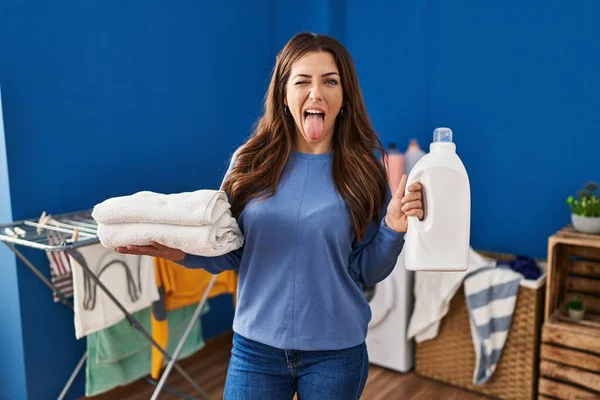 Młoda Brunetka Kobieta Trzyma Czyste Pranie Butelkę Detergentu Wystający Język — Zdjęcie stockowe