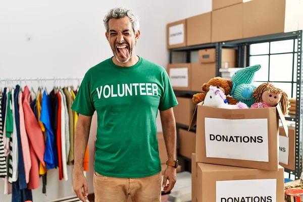 Bağışlarda gönüllü tişört giyen orta yaşlı İspanyol adam komik bir ifadeyle dilini dışarı çıkarıyor. duygu kavramı. 