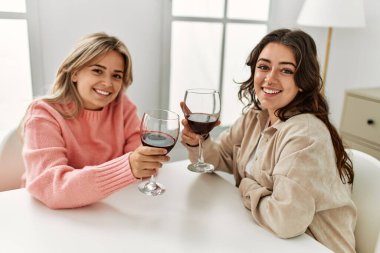 Genç çift mutlu bir şekilde kadeh kaldırıyor kırmızı şarap kadehiyle evde..