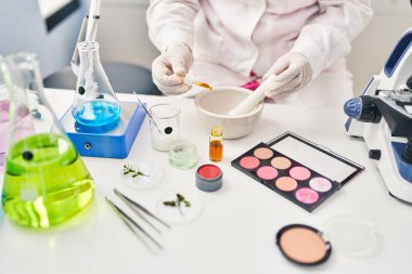 Genç İspanyol kadın bilim adamı üniforması giyiyor. Laboratuvarda kaseye sıvı döküyor.