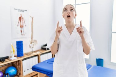 Ağrı giderme kliniğinde çalışan beyaz bir kadın şaşkın şaşkın yukarı bakıyor ve parmaklarıyla işaret edip kollarını kaldırıyordu.. 