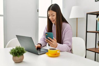 Laptop ve akıllı telefon kullanan Çinli genç bir kız evdeki masada oturuyor..