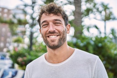 Genç İspanyol adam parkta yürürken kendinden emin gülümsüyor.
