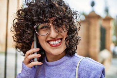 Orta Doğulu genç bir kadın gülümsüyor. Akıllı telefondan konuşuyor.