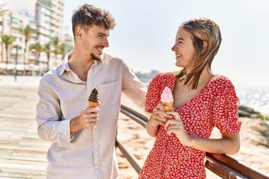 Genç İspanyol çift tatilde gülümseyerek kumsalda dondurma yiyor.