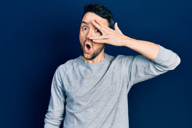 Gündelik kıyafetler giyen genç İspanyol adam şok içinde yüzünü ve gözlerini kapayarak utanmış ifadesiyle parmaklarından bakıyor.. 