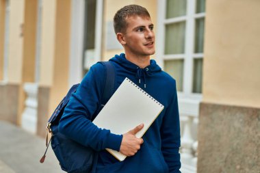 Üniversitede elinde defterle gülümseyen sarışın genç bir öğrenci..