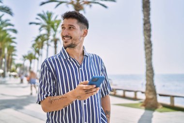 Genç yakışıklı adam deniz kenarında akıllı telefon kullanıyor.