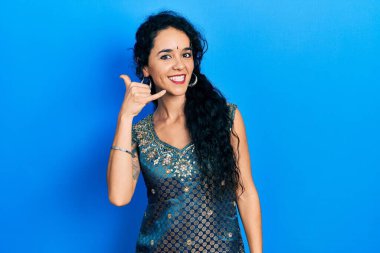 Bindi giyen ve geleneksel kurta elbisesi giyen genç bir kadın telefonla el ve parmak hareketleriyle gülümsüyor telefonda konuşuyor gibi. iletişim kavramları. 