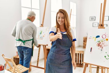Resim stüdyosunda önlük giymiş İspanyol bir kadın selamlaşma ve dostça bir şekilde el sıkışırken gülümsüyor. başarılı iş. 