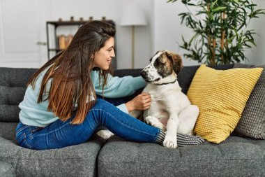 Genç bir kadın evdeki kanepede oturan köpeğe sarılıyor.