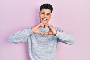 Gündelik kıyafetler giyen, aşık gülümseyen, elleriyle kalp sembolü yapan genç bir İspanyol. romantik kavram. 