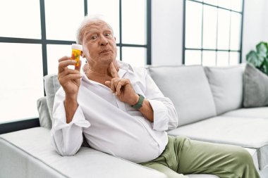 Elinde haplar olan kıdemli bir adam şüphe üzerine yoğunlaşmıştı. Parmakları çenesinde ve yukarı bakıyordu. 