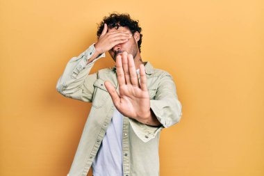 Latin kökenli genç bir adam, günlük kıyafetler giyip, elleriyle gözlerini kapatıyor ve üzgün ve korku ifadeleriyle jestleri durduruyor. utangaç ve olumsuz kavram. 