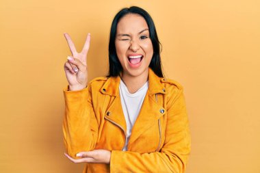 Burnuna piercing takan, sarı deri ceket giyen, gülümseyen, kameraya göz kırpan, parmaklarıyla zafer işareti yapan güzel İspanyol kadın. İki numara.. 