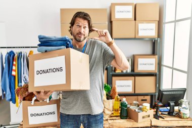 Gönüllü olarak bağış kutusunu tutan yakışıklı, orta yaşlı bir adam gülümseyen ve kendine güvenen, el hareketi yapan, parmakları küçük gösteren ve kameraya bakan biri. ölçüm kavramı. 