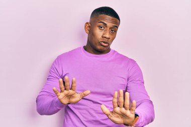 Genç siyah bir adam pembe bir kazak giyiyor. Avuçlarını hareket ettiriyor. Korkmuş ve iğrenç bir ifadeyle reddediyor. Dur ve yasakla. 