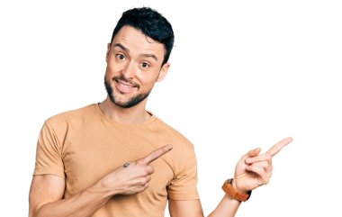 Sakallı, sıradan tişörtlü, gülümseyen ve kameraya bakan iki eli ve parmakları yandan gösteren İspanyol bir adam.. 