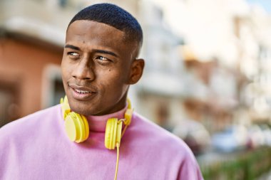 Genç Afrikalı Amerikalı adam şehirde kulaklık takarak mutlu bir şekilde gülümsüyor..