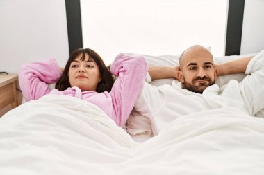 Genç İspanyol çift gülümsüyor, mutlu, elleri yatak odasının üstünde rahatlamış..