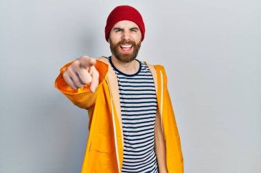 Sakallı, sarı yağmurluk giyen beyaz bir adam kameraya karşı kızgın ve sinirli. 