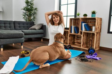 Genç beyaz kadın gülümsüyor evde köpekle esniyor.