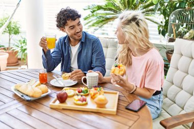 Genç çift, mutlu bir şekilde gülümsüyor. Kahvaltıyı terasta yapıyorlar..