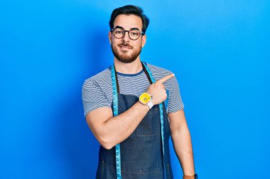 Sakal terzisi olan yakışıklı beyaz adam atölye önlüğü giyiyor. Gülümsüyor, eli ve parmağı yan tarafta. 