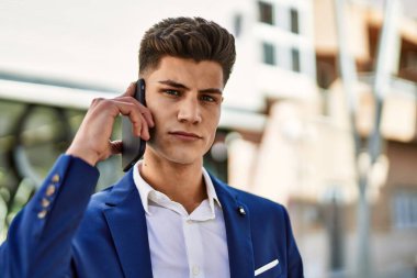 Akıllı telefondan konuşan genç adam sokakta takım elbise giyiyor.