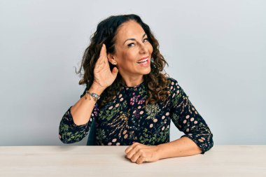 Gündelik giysiler giymiş güzel orta yaşlı bir kadın masaya oturmuş, ağzı kulaklarında oturmuş dedikoduları ve dedikoduları dinliyor. Sağırlık kavramı. 