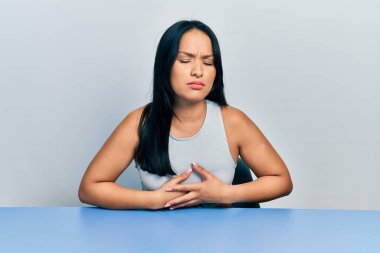 Burnunda piercing olan güzel bir İspanyol kadın elleri karnında masada oturuyor çünkü hazımsızlık, acı verici bir hastalık kendini iyi hissetmiyor. Ağrı kavramı. 