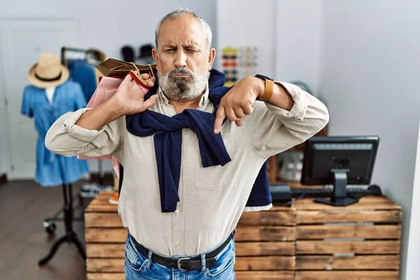 Butik dükkanında alışveriş torbaları tutan yakışıklı bir adam üzgün ve üzgün görünüyor, parmaklarıyla yönü gösteriyor, mutsuz ve depresif.. 